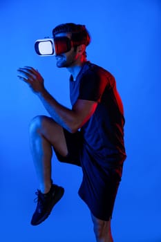 Caucasian smart man jogging while wearing VR goggle with neon light. Happy person with casual cloth running or exercising while using virtual reality headset. Innovation technology concept. Deviation.