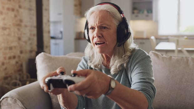 Confused, senior woman and headphones for video game, online streaming and relax for retirement at home. Tech, elderly person and frustrated with joystick for esports, gaming and challenge on sofa.