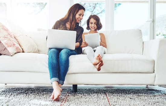 Laptop, tablet and mother with child on sofa for streaming movies, happiness and bonding together in living room. Family, mom and young girl with technology for watching videos, film or relax in home.