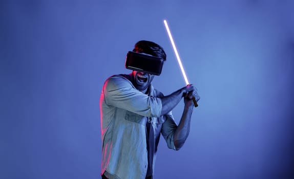 Caucasian man wearing VR glass and moving gesture holding sword. Gamer using future digital virtual reality headset or futuristic innovation to enter meta world or playing action game. Deviation.
