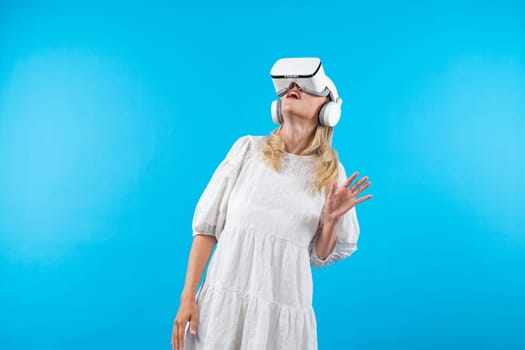 Girl with VR goggles looking around at hologram world. Woman surprised to connect metaverse by using visual reality world and standing at blue background. Innovation technology concept. Contraption.
