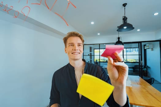 Professional caucasian businessman writing marketing idea by using mind map and sticky notes on glass board at modern meeting room. Creative business and planing concept. Closeup. Immaculate.