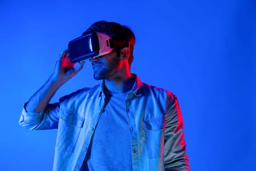 Caucasian man enter metaverse by using virtual digital goggles while standing look in cyberspace display virtual world. Sport gamer with casual cloth move gesture at neon background. Tech. Deviation.