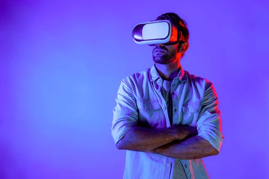 Smart caucasian man using virtual reality glass while crossing arm with confident. Professional happy teenager with casual cloth standing with folded arm colorful at neon light background. Deviation.