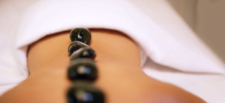 Spa, treatment and rock on back for woman, stress relief and pain or muscle tension help. Relax, luxury and zen for body care and wellness service, holistic and beauty salon with stones for detox.