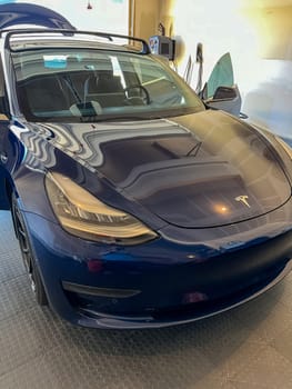 Castle Rock, Colorado, USA-March 14, 2024-A shiny blue Tesla Model 3 sits in the well-kept garage of a single-family house, its sleek design accentuated by the gentle care of a home car wash.