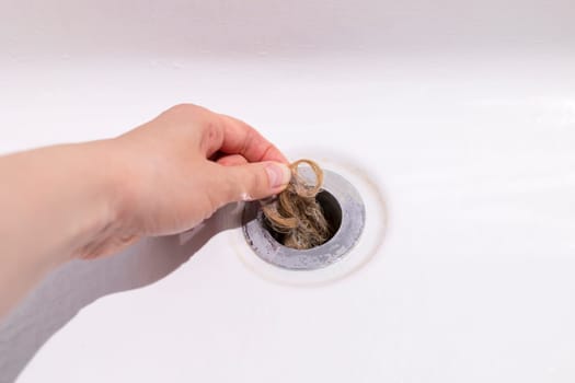 Clogs In Drain, Hair Loss, Hair Fall. Human Hand Pulls Big Tuft Of Blond Hair In White Bathtub Of Bathroom, Shower. Clogged Pipe. Plumbing Difficulties At Home. Thin Hair Problem. Horizontal Plane.
