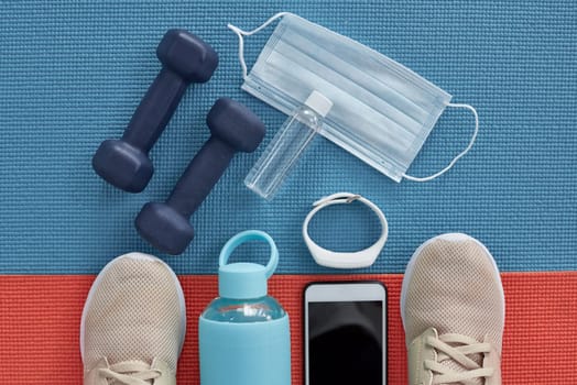 Workout, equipment and face mask on yoga mat with tech for fitness tracker and gym progress. Above, floor and wellbeing for illness prevention at health and wellness club for sport with weights.