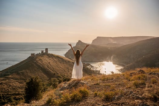woman stands on a hill overlooking the ocean, her arms raised in the air. Concept of freedom and joy, as if the woman is celebrating a moment of happiness or accomplishment