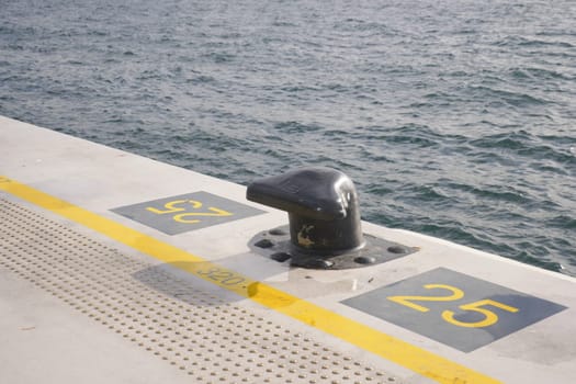 A black mooring bollard on the edge of a concrete pier