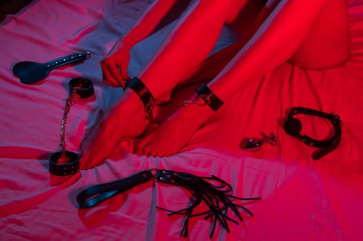 Close-up of female legs in chains on the bed in neon red-blue light. BDSM concept