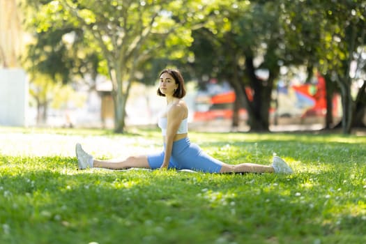A woman is doing a split on a grassy field. Concept of freedom and relaxation, as the woman is stretching her body in a natural setting