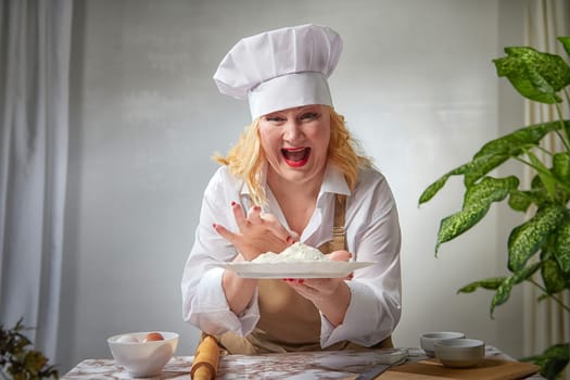 A fat funny female cook in a hat and apron poses in the kitchen and takes selfie. Good cooking and body positive