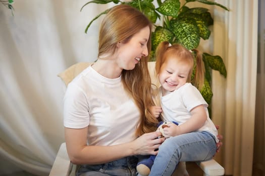 Happy loving family. Mother and daughter child girl playing and hugging in living room with wicker chair