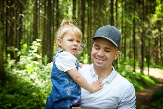 Gentle Father Holding Young Daughter Outdoors in Daylight. A tender moment as dad embraces his little girl in a sunny garden