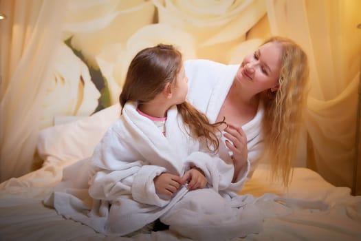 Mother and daughter happily relax and fun together on bed in bedroom. The concept of tenderness between mom and girl