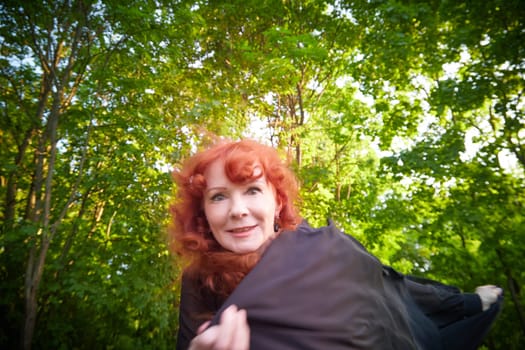 Elegant senior mature Woman dancing in Black Dress in green park. Woman with red hair posing on nature