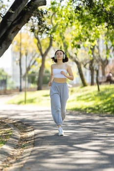 A woman is running on a path in a park. She is wearing headphones and is listening to music