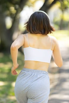 A woman is running in a park. She is wearing a white tank top and gray pants. Concept of energy and movement, as the woman is enjoying her run. The park setting adds a natural