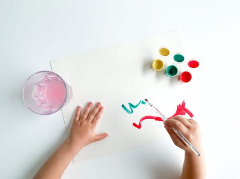 small child draws with paints and brush on white table. High quality photo