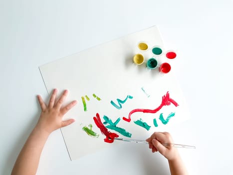 small child draws with paints and brush on white table. High quality photo