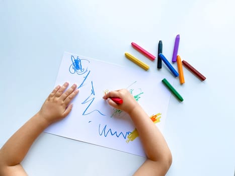 small child draws with pastel crayons on white table. High quality photo