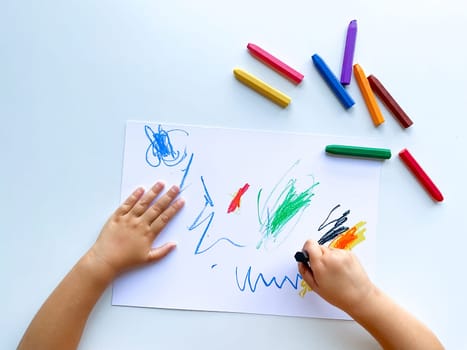 small child draws with pastel crayons on white table. High quality photo