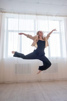 Caucasian woman dances contemporary in ballet class. Dancer in a jump. Vertical photo