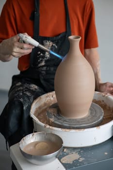 Close-up of a potter's hands firing a jug with a gas burner on a potter's wheel. Vertical photo