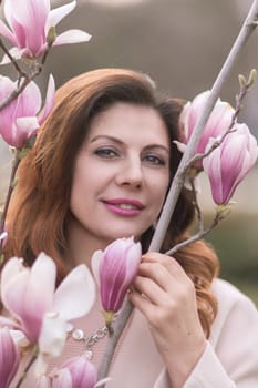 Woman magnolia flowers, surrounded by blossoming trees, hair down, wearing a light coat. Captured during spring, showcasing natural beauty and seasonal change