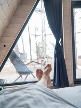 A man's feet sticking out from under a blanket in a country house with panoramic windows. Vertical photo