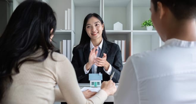 A real estate agent or insurance agent presents a house plan and insurance contract to an Asian couple..