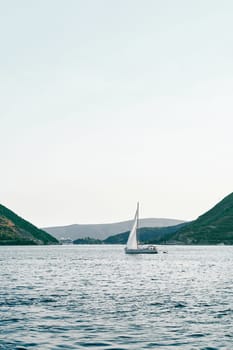 White small sailing yacht sails on the sea along the mountainous coast. High quality photo