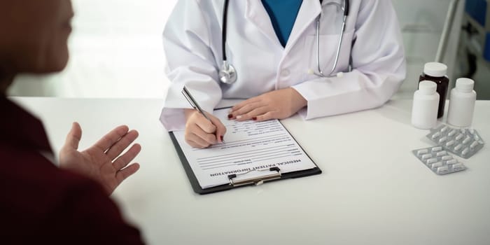 Doctor consulting male elderly patient filling medical form. Professional physician writing information in clipboard checking examining elderly man during appointment visit in clinic.