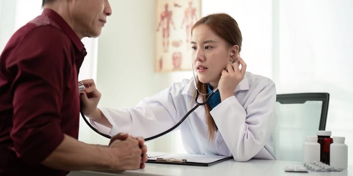 Female doctor asian cardiologist examining senior male cardiac patient listening checking heartbeat using stethoscope at checkup hospital visit. elderly healthcare cardiology concept.