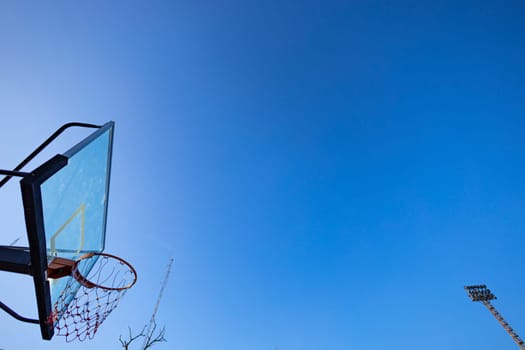 Basketball hoop over the blue sky and sport light pole.