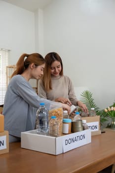 Donation and two woman volunteer asian of happy packing food in box at home. Charity.