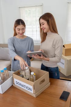 Donation and two woman volunteer asian of happy packing food in box at home. Charity.