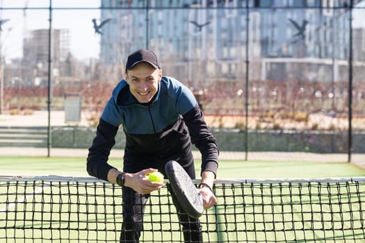 A padel player jump to the ball, good looking for posts and poster. Man with black racket playing a match in the open behind the net court outdoors. Professional sport concept with space for text. High quality photo