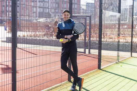 Portrait of positive young man with racket and padel ball on tennis court. High quality photo