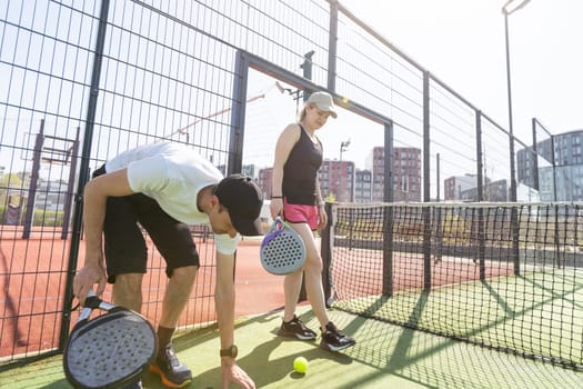 Sports couple with padel rackets posing on tennis court. High quality photo