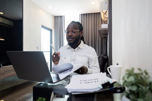 African American man working with laptop computer remote while sitting at glass table in living room. Black guy do freelance work at home office.