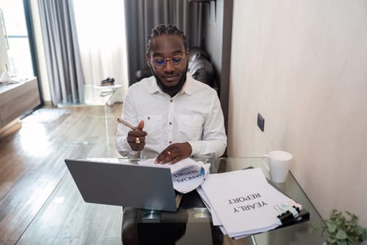 African American man working with laptop computer remote while sitting at glass table in living room. Black guy do freelance work at home office.