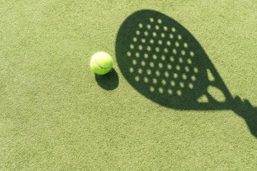 Shadow of a padel racket with a yellow ball on the green grass. High quality photo