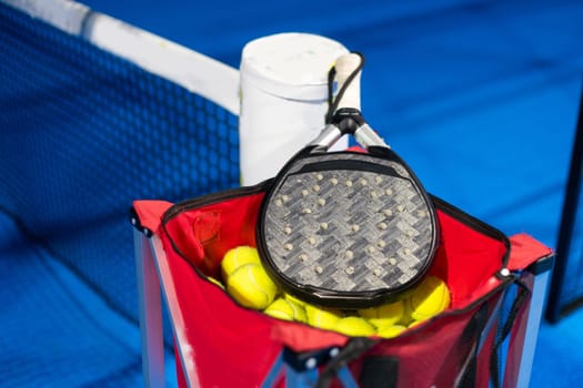 Black professional paddle tennis racket and ball with natural lighting on blue background. Horizontal sport theme poster, greeting cards, headers, website and app. High quality photo