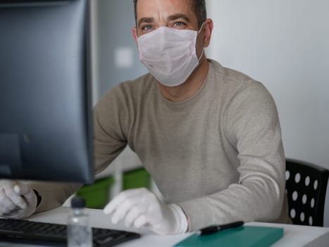 Young woman wearing protective gloves on hands and mask on face working from office or home using laptop on desk. Preventing corona virus covid-19 spread during epidemic outbreak