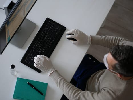 Young woman wearing protective gloves on hands and mask on face working from office or home using laptop on desk. Preventing corona virus covid-19 spread during epidemic outbreak. top view from above