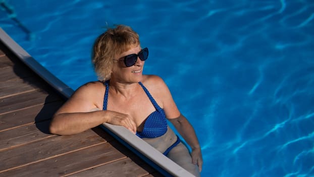 An elderly woman in sunglasses swims in the pool. Vacation in retirement