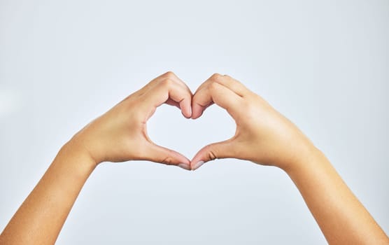 Hands, closeup and person in studio with heart sign, gesture or symbol isolated on white background. Zoom, love and care icon with romance emoji for compassion, kindness and happiness for valentines.
