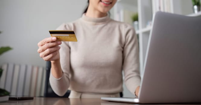 Beautiful young woman uses laptop to shop online, buys things and pays with credit card through phone online banking app..